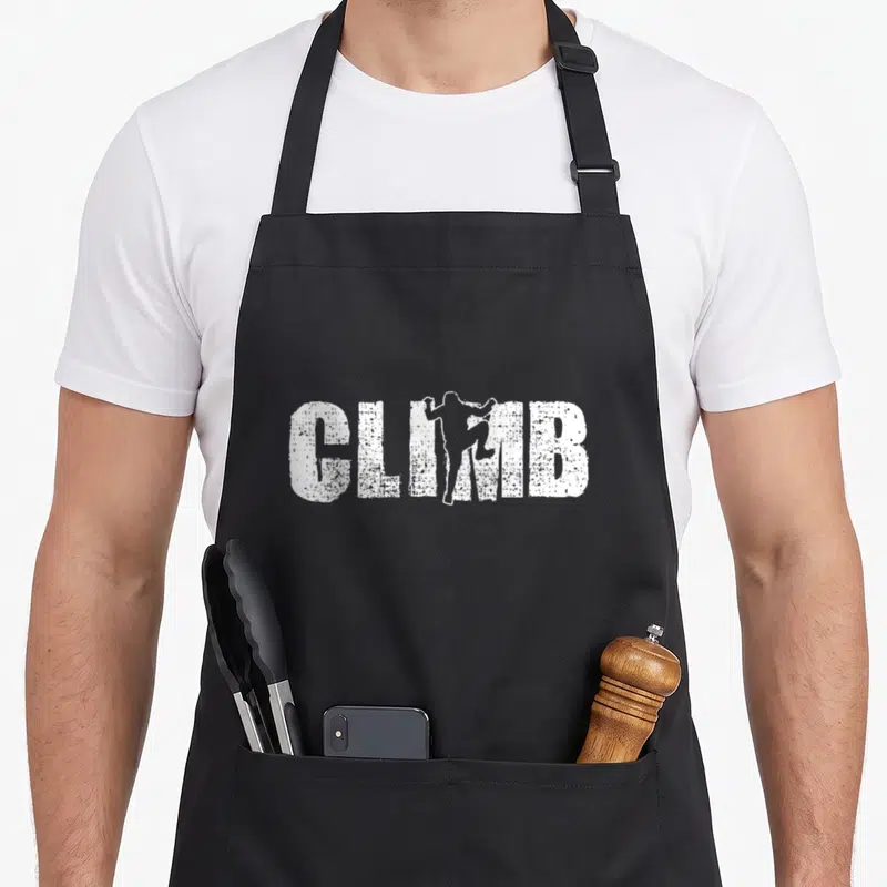 Climbing bouldering addict apron - White distressed CLIMB text with climber silhouette replacing the letter I — shown on a black cotton canvas apron against a white background