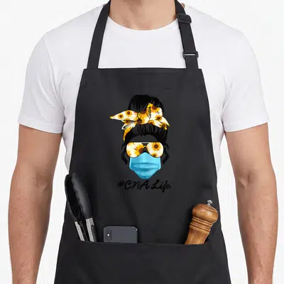 Costume nurse apron - Cartoon woman with sunflower bow, sunglasses, blue mask, and #CNA Life text — shown on a black cotton canvas apron against a white background