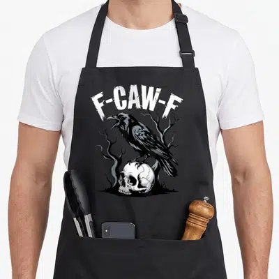 Skull bird aprons - F-Caw-F text arching over a crow perched on a skull among dead trees — shown on a black cotton canvas apron against a white background