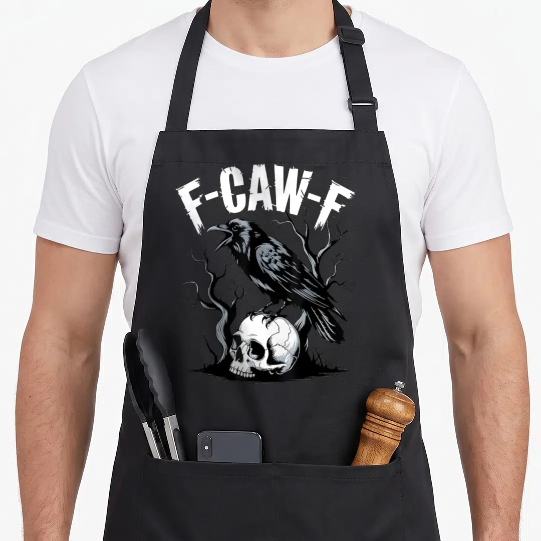 Skull bird aprons - F-Caw-F text arching over a crow perched on a skull among dead trees — shown on a black cotton canvas apron against a white background