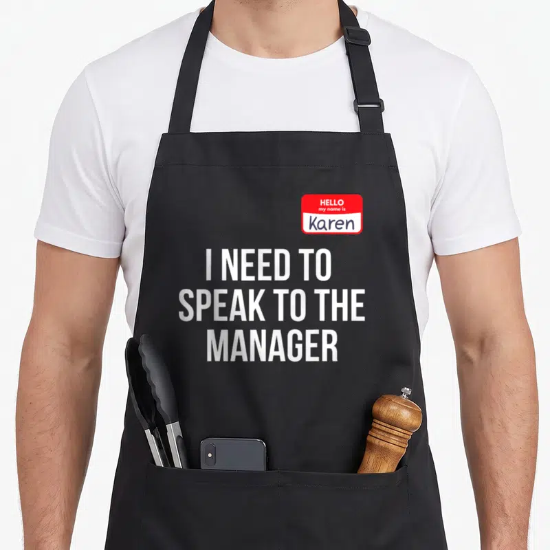 Speak manager halloween apron - Red name tag reading Hello my name is Karen above three lines of white text I need — shown on a black cotton canvas apron against a white background