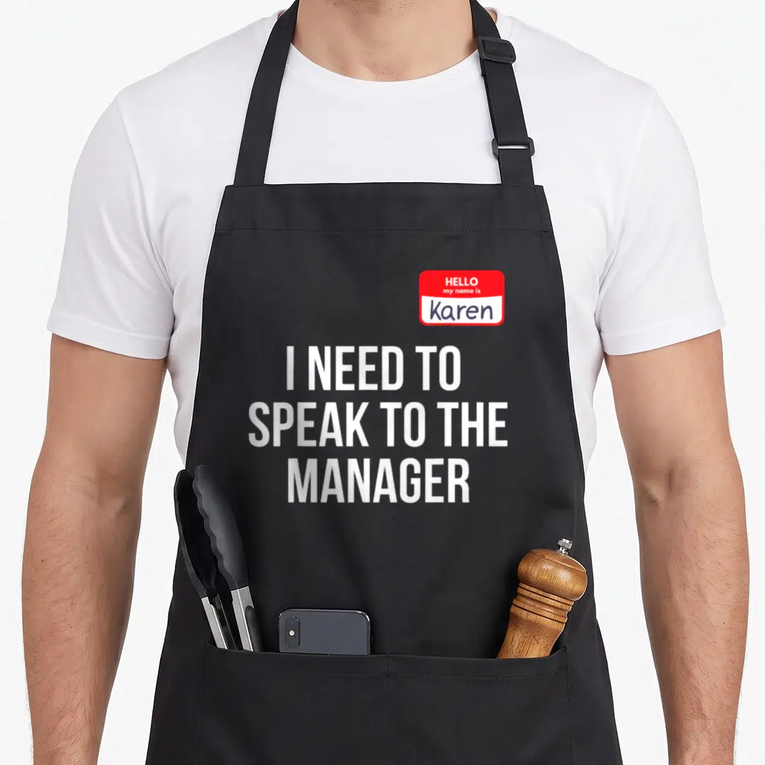 Speak manager halloween apron - Red name tag reading Hello my name is Karen above three lines of white text I need — shown on a black cotton canvas apron against a white background