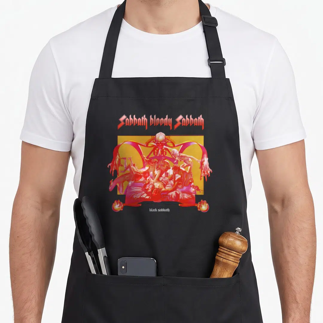 Bright bloody apron - Sabbath bloody Sabbath text above red skeletal demon scene on yellow background — shown on a black cotton canvas apron against a white background
