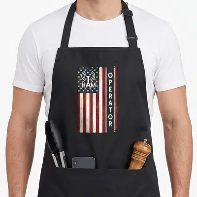 Ham 4th of july apron - Distressed US flag with HAM text on canton and vertical OPERATOR next to radio tower icon — shown on a black cotton canvas apron against a white background