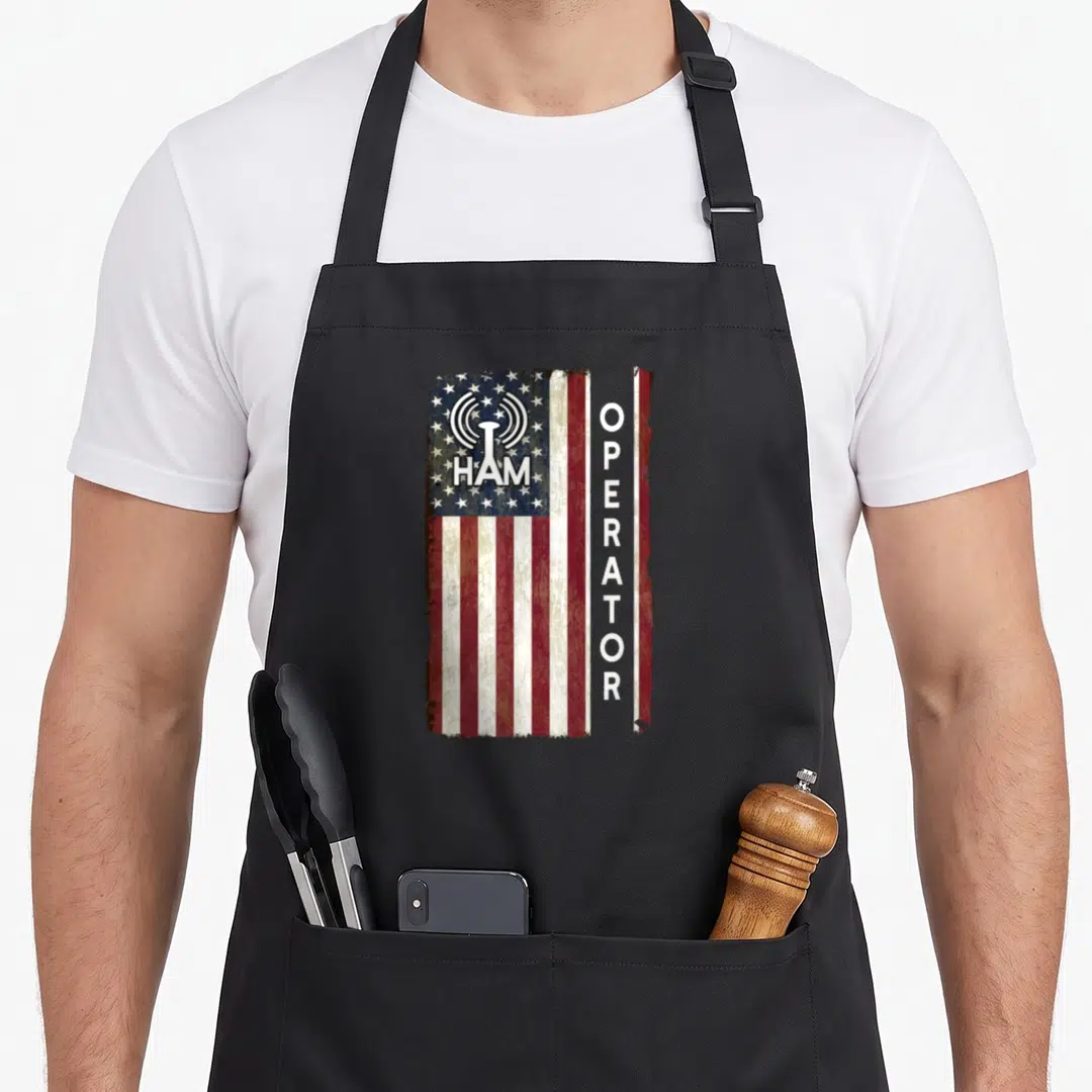 Ham 4th of july apron - Distressed US flag with HAM text on canton and vertical OPERATOR next to radio tower icon — shown on a black cotton canvas apron against a white background