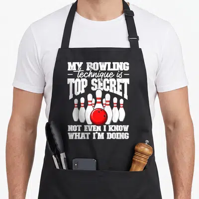 Bowling secret dad apron - Red bowling ball in front of six white pins with white top secret text — shown on a black cotton canvas apron against a white background