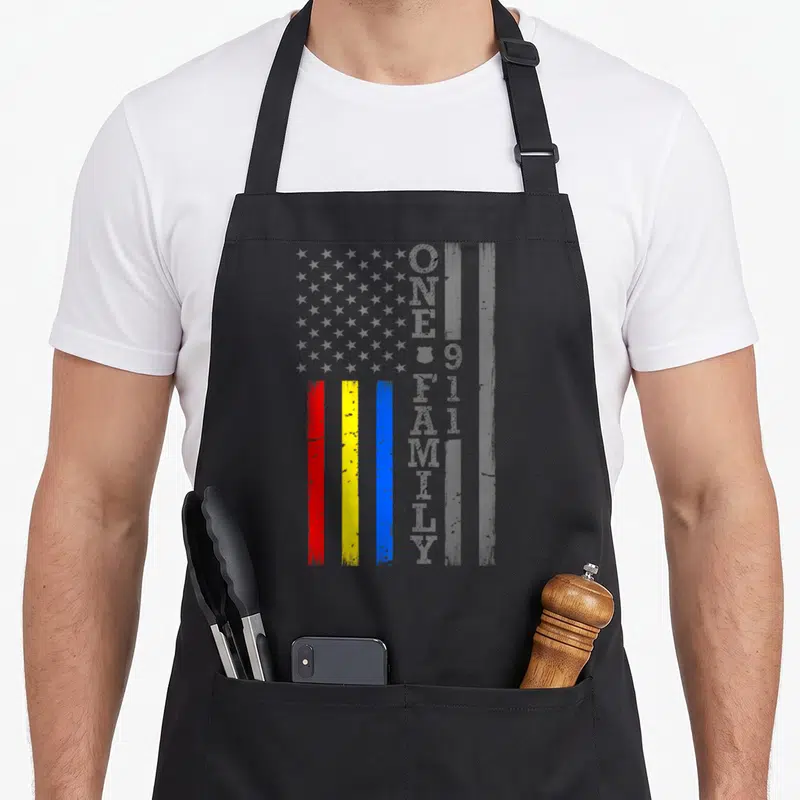 Fire service apron - Distressed grey flag with red yellow blue stripes and vertical One Big Family 911 text — shown on a black cotton canvas apron against a white background