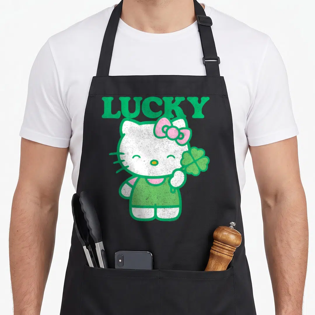 Clover lucky apron - Hello Kitty standing holding four-leaf clover under LUCKY text in green and pink — shown on a black cotton canvas apron against a white background