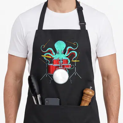 Octopus drum kit apron - Cartoon blue octopus playing red drum kit with yellow cymbals — shown on a black cotton canvas apron against a white background