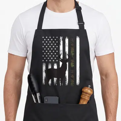 Whitetail camo aprons - Black deer silhouette in front of distressed American flag with one green camouflage vertical — shown on a black cotton canvas apron against a white background