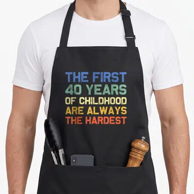 Childhood 40th birthday apron - Stacked text reading The First 40 Years Of Childhood Are Always The Hardest in blue — shown on a black cotton canvas apron against a white background