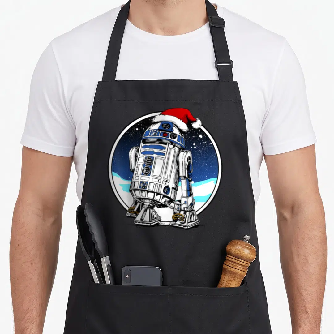 Circle santa aprons - R2-D2 in circular frame wearing red Santa hat against starry blue sky and snow — shown on a black cotton canvas apron against a white background