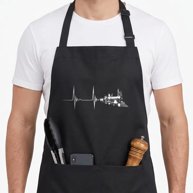 Heartbeat steam locomotive apron - White heartbeat line transitioning into a black steam locomotive illustration — shown on a black cotton canvas apron against a white background