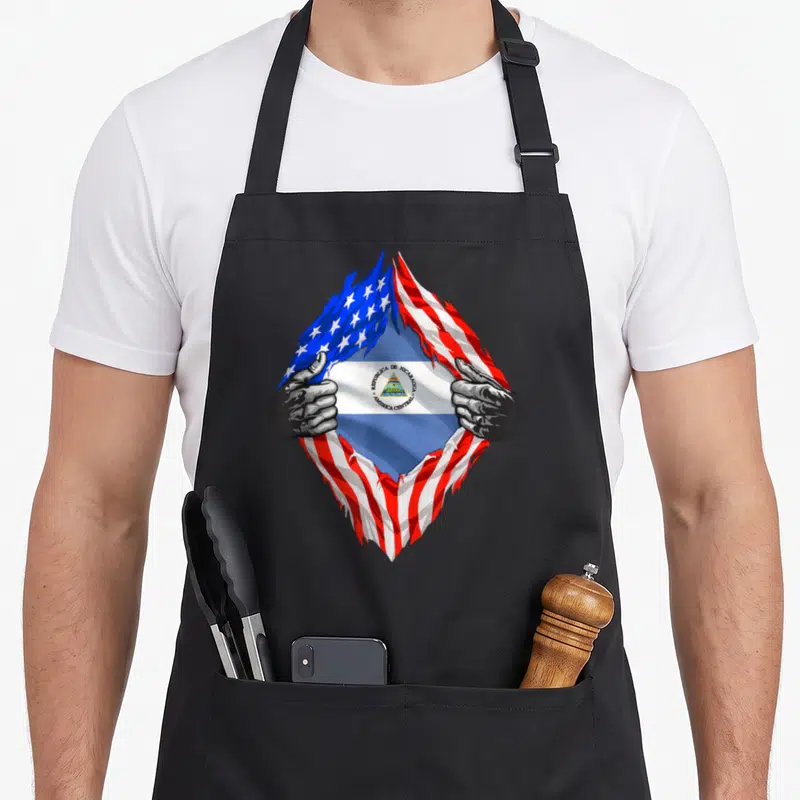 Nicaragua american flag apron - Hands tearing USA flag to reveal Nicaragua flag with REPUBLICA DE NICARAGUA text — shown on a black cotton canvas apron against a white background