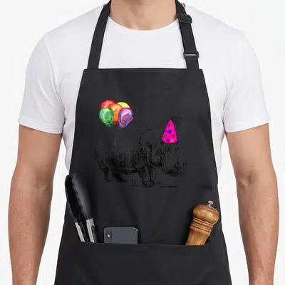 Hippo balloon apron - Grey hippo with pink party hat and five colorful balloons in watercolor style — shown on a black cotton canvas apron against a white background