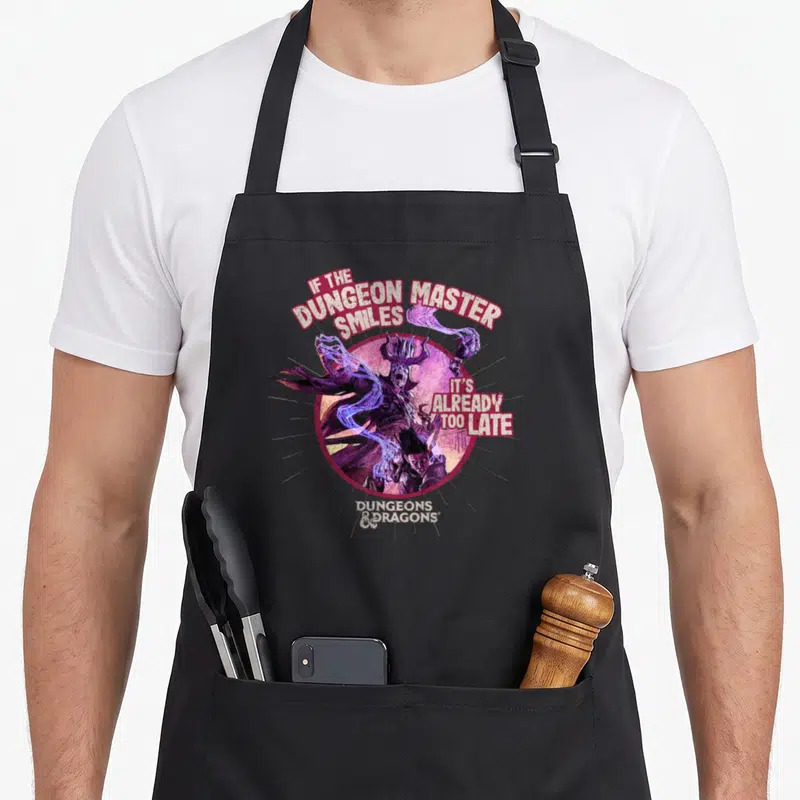 Smile master apron - Dungeon Master illustration with If the Dungeon Master Smiles text in purple and red circle — shown on a black cotton canvas apron against a white background
