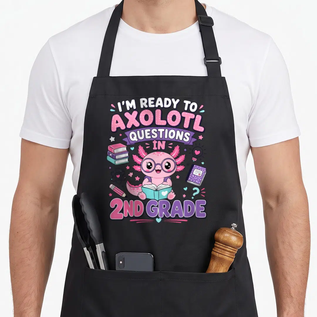 Axolotl 2nd apron - Cartoon pink axolotl reading book surrounded by stacked books, notebook, lightbulb, and text 'I'M — shown on a black cotton canvas apron against a white background