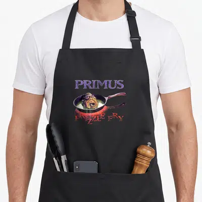 Primus fries apron - Monster head in green liquid inside frying pan with PRIMUS FRIZZLE FRY text — shown on a black cotton canvas apron against a white background