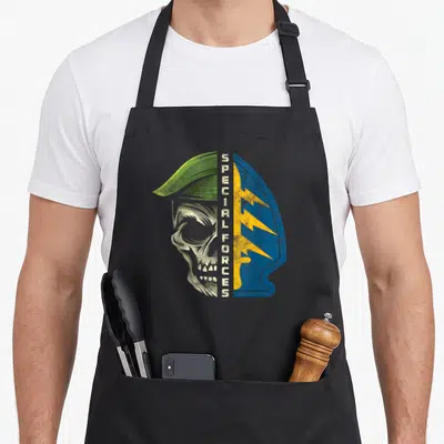 Army special aprons - Distressed skull profile split by vertical text next to blue shield with yellow lightning bolts — shown on a black cotton canvas apron against a white background