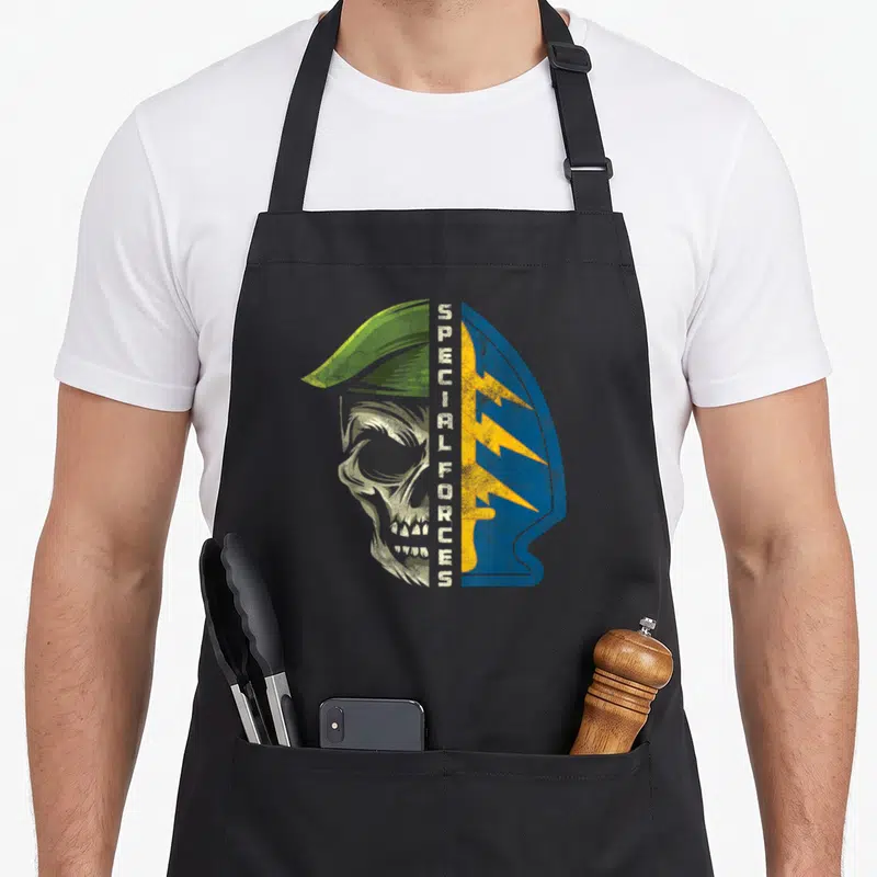 Army special aprons - Distressed skull profile split by vertical text next to blue shield with yellow lightning bolts — shown on a black cotton canvas apron against a white background