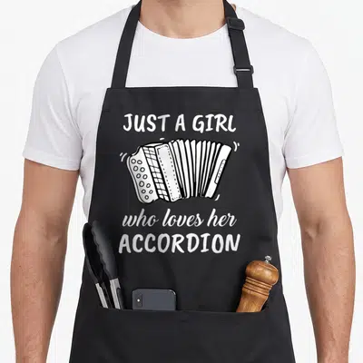 Cute accordion apron - White line-art accordion centered between three lines of text reading JUST A GIRL who loves — shown on a black cotton canvas apron against a white background