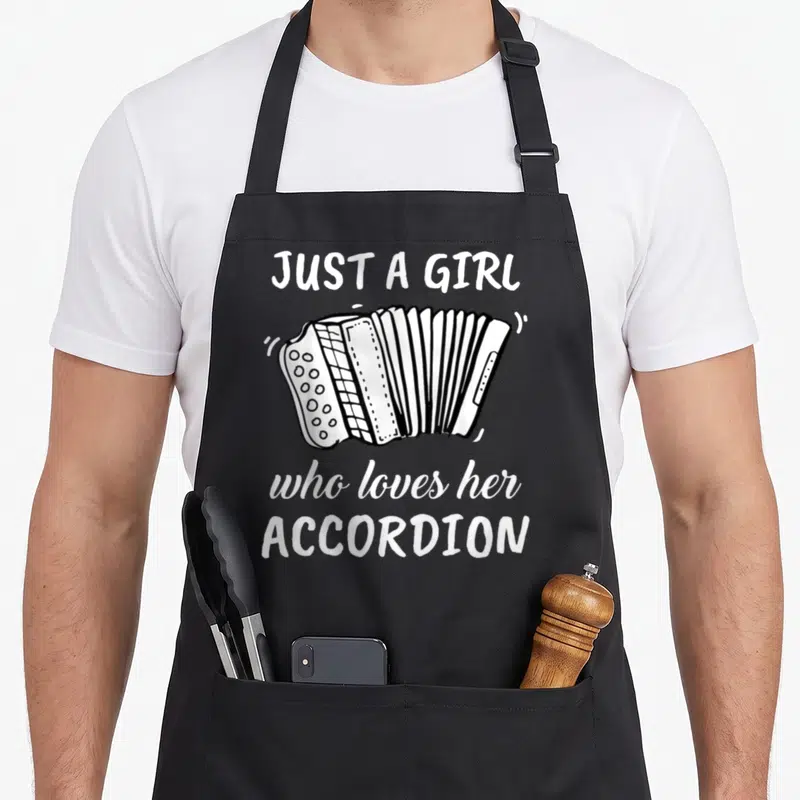 Cute accordion apron - White line-art accordion centered between three lines of text reading JUST A GIRL who loves — shown on a black cotton canvas apron against a white background