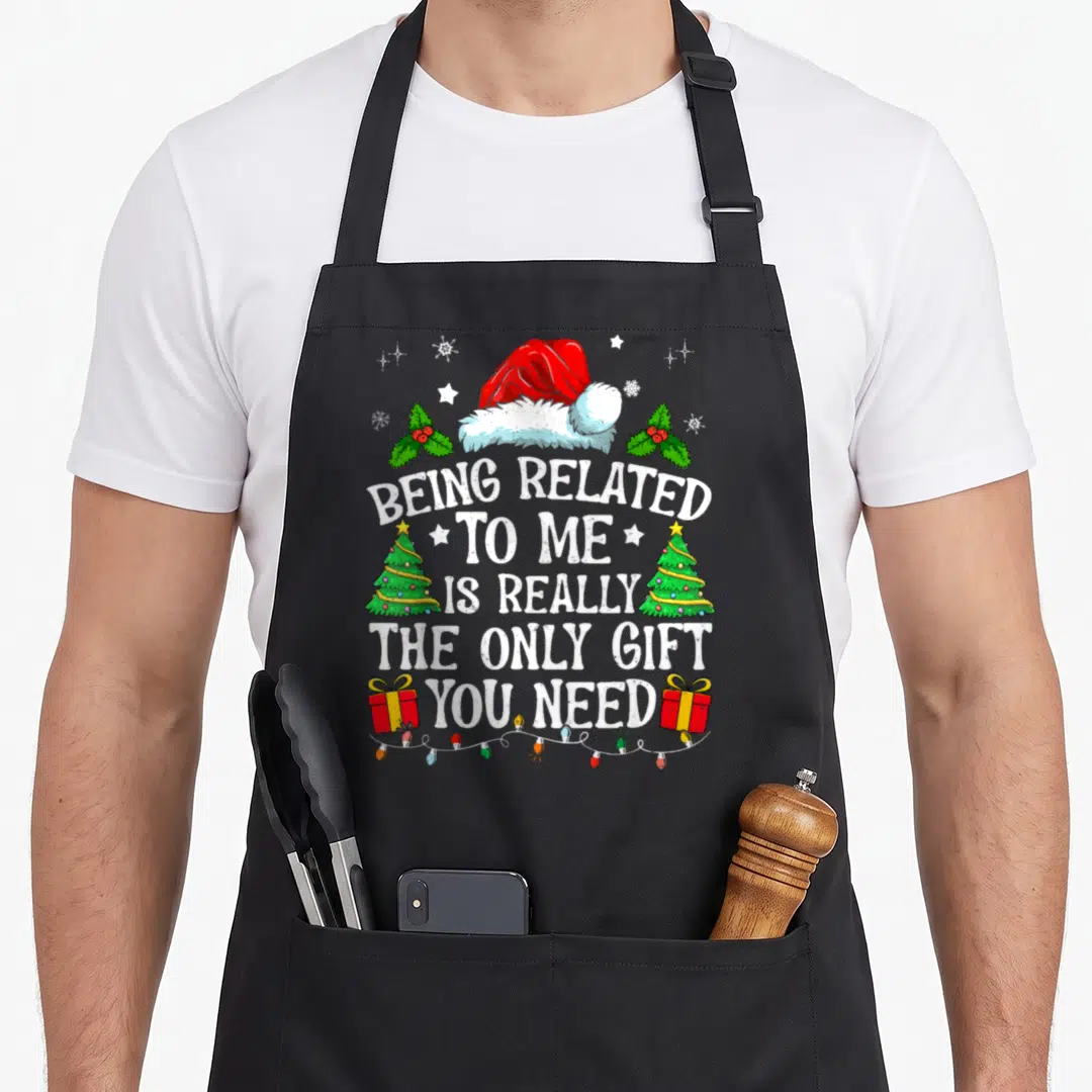 Related sleepover apron - Santa hat holly trees gifts text Being Related To Me Is The Only Gift You Need — shown on a black cotton canvas apron against a white background