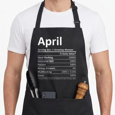 Nutrition april apron - April nutrition facts label with percentages for hard work, multitasking, and sass in white text — shown on a black cotton canvas apron against a white background