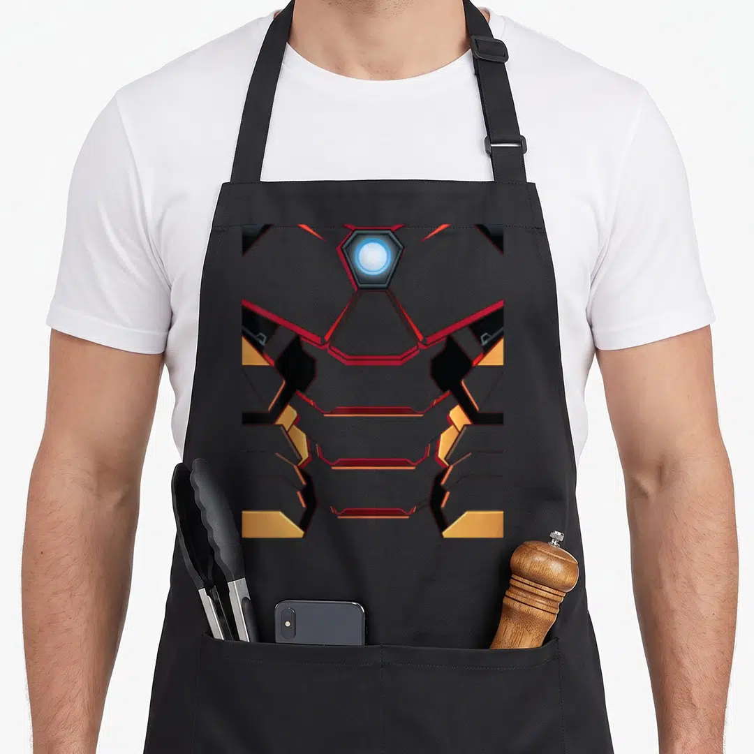 Tony ironman apron - Grey mechanical chest armor with glowing blue light and red gold geometric accents — shown on a black cotton canvas apron against a white background
