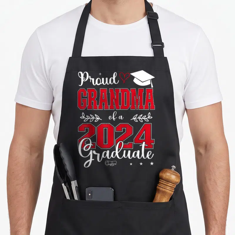 Class grandma apron - Stacked red and white text reading Proud Grandma 2024 Graduate with cap heart and diploma graphics — shown on a black cotton canvas apron against a white background