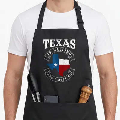 Calling must texas apron - Retro Texas map in blue white and red with arched text and two white ribbons containing — shown on a black cotton canvas apron against a white background
