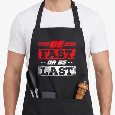 Fast drag car apron - Stacked text reading BE FAST OR BE LAST in red and white distressed blocks with grey lettering — shown on a black cotton canvas apron against a white background