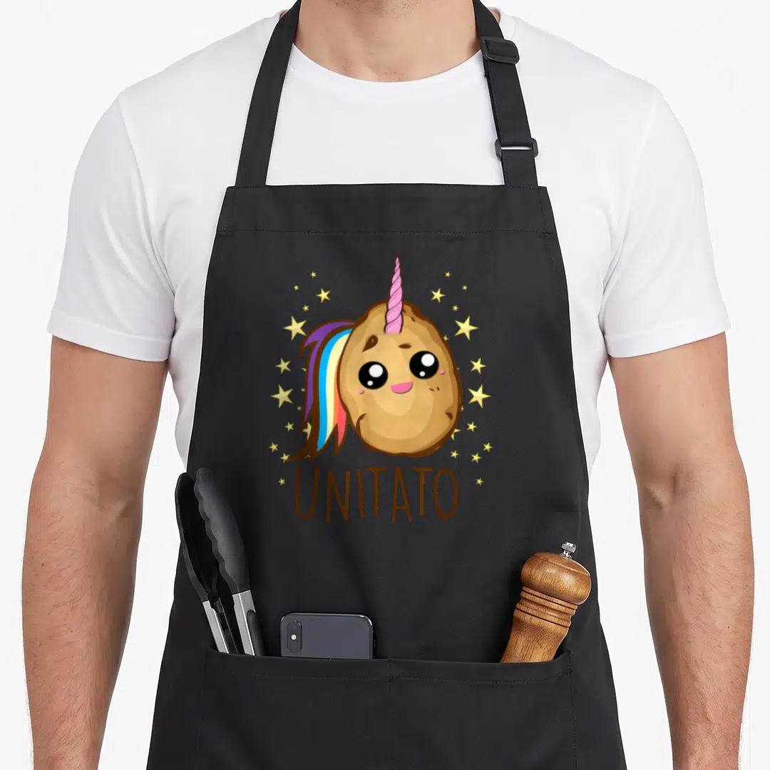 Unicorn potato apron - Cartoon brown potato with pink horn, rainbow mane, yellow stars, and UNITATO text below — shown on a black cotton canvas apron against a white background