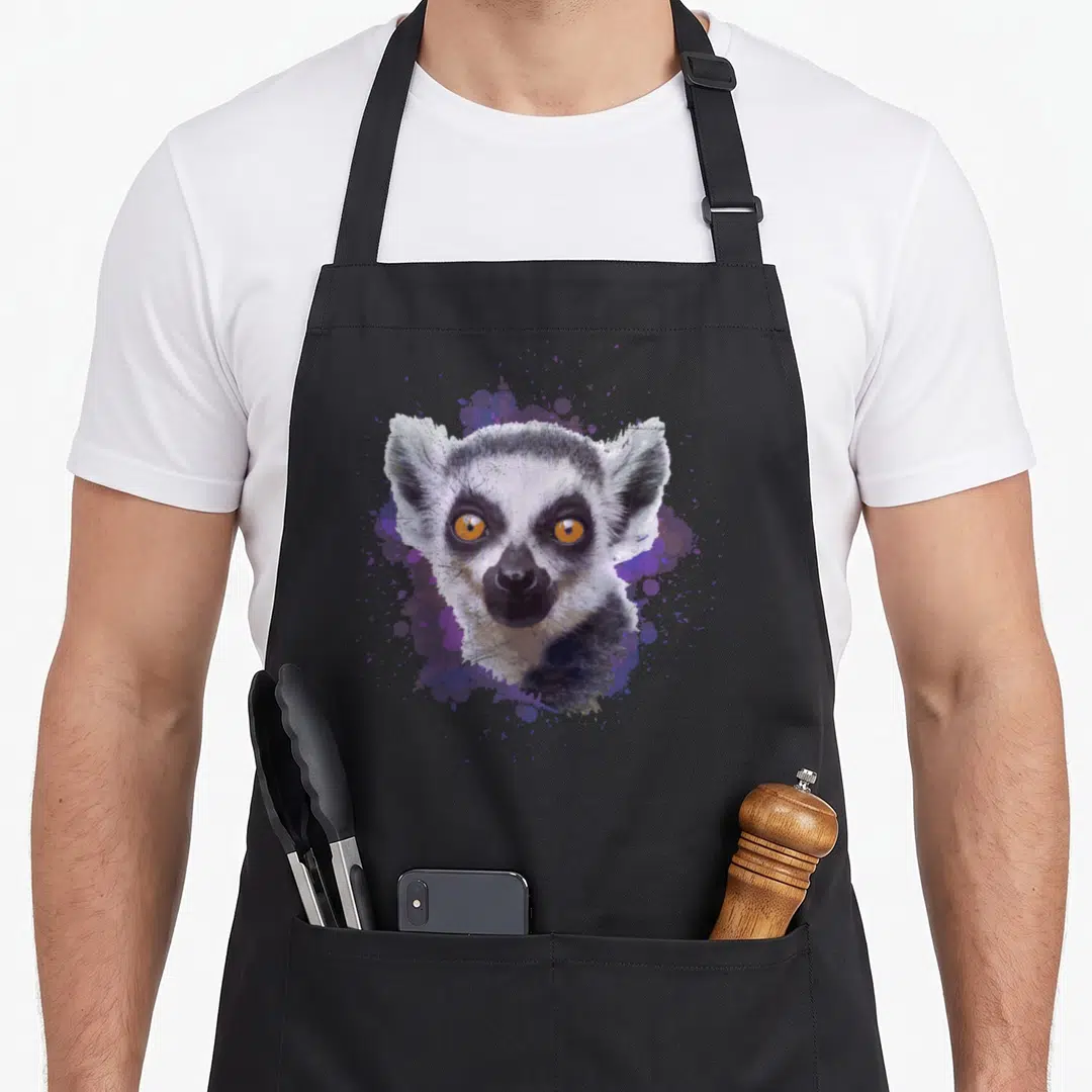 Animal lemur apron - Realistic lemur head with orange eyes over purple and blue watercolor splatter — shown on a black cotton canvas apron against a white background