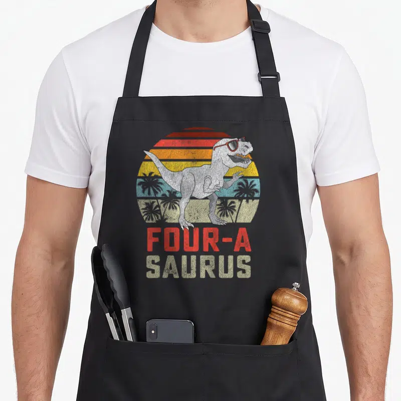 Four t-rex apron - T-Rex in sunglasses standing before a striped retro sunset with stacked text below — shown on a black cotton canvas apron against a white background