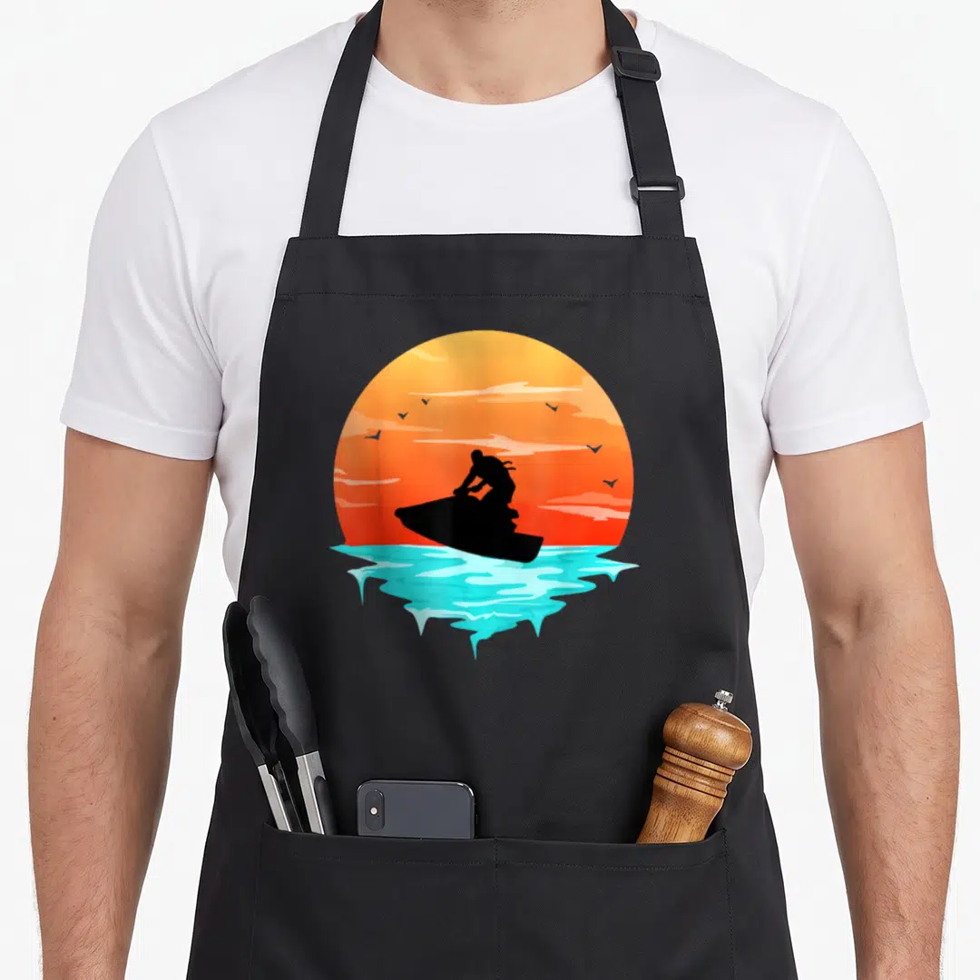 Swimmer racing apron - Black jet ski silhouette against orange sun and cyan water splash with birds — shown on a black cotton canvas apron against a white background