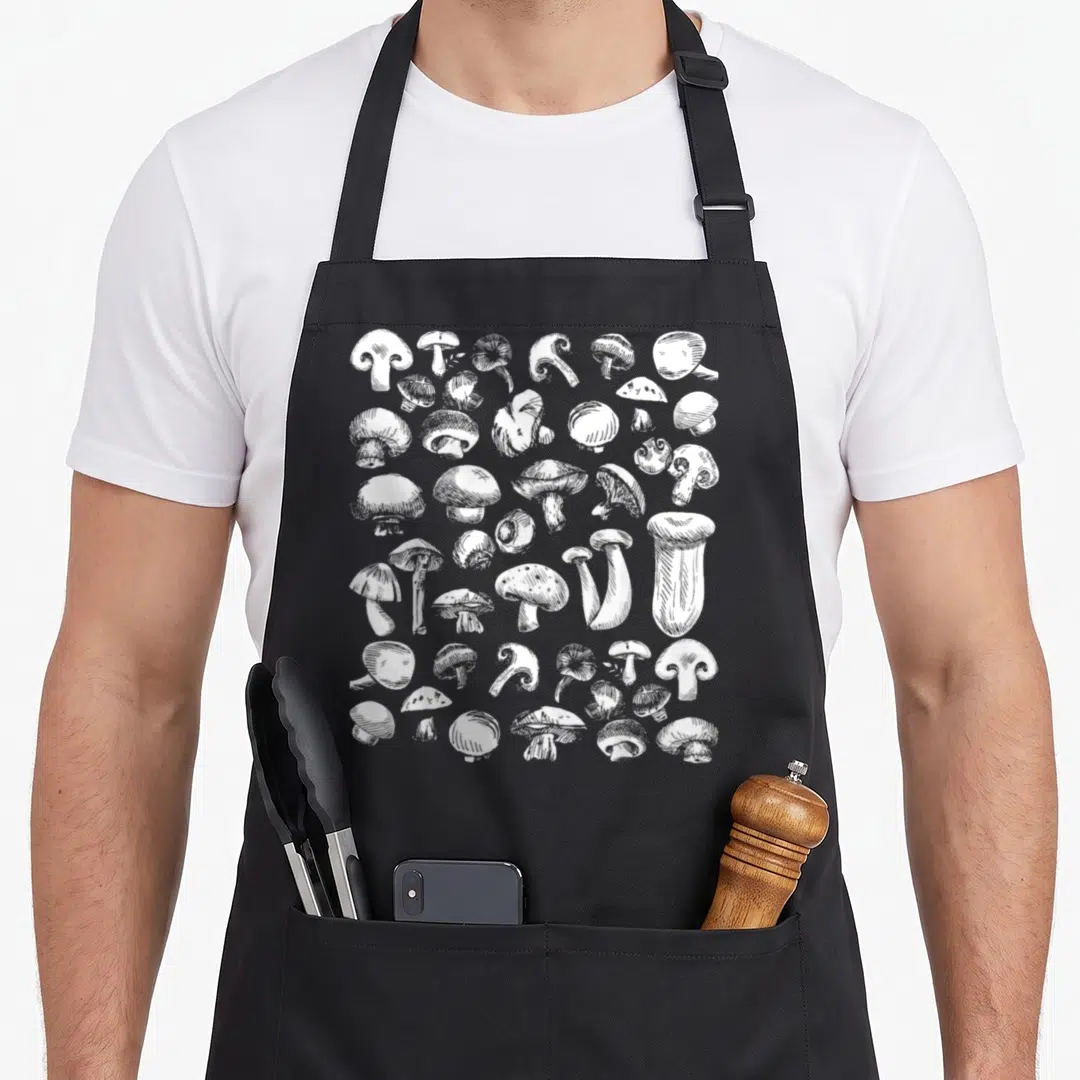 Fungiphile foraging apron - White line-art cluster of various mushroom species scattered across fabric — shown on a black cotton canvas apron against a white background