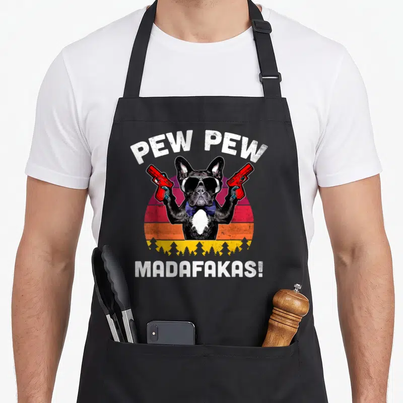 Pew french bulldog apron - Cartoon french bulldog holding red guns in front of a retro sunset with arched text — shown on a black cotton canvas apron against a white background
