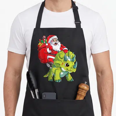Triceratop christmas santa apron - Cartoon Santa riding green triceratops holding red sack and candy cane — shown on a black cotton canvas apron against a white background