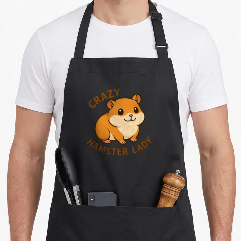 Retro hamster animal apron - Cartoon hamster with arched CRAZY HAMSTER LADY text in orange and brown — shown on a black cotton canvas apron against a white background