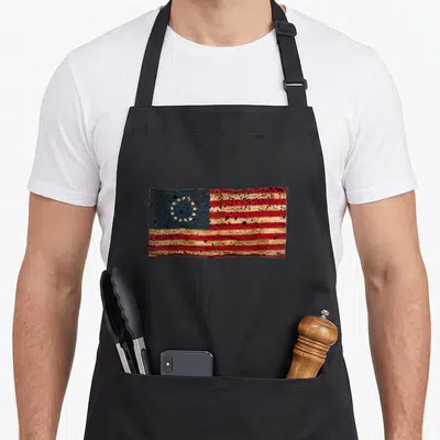 Trend distressed apron - Betsy Ross flag with 13 stars in a circle, red white blue stripes, distressed splattered — shown on a black cotton canvas apron against a white background
