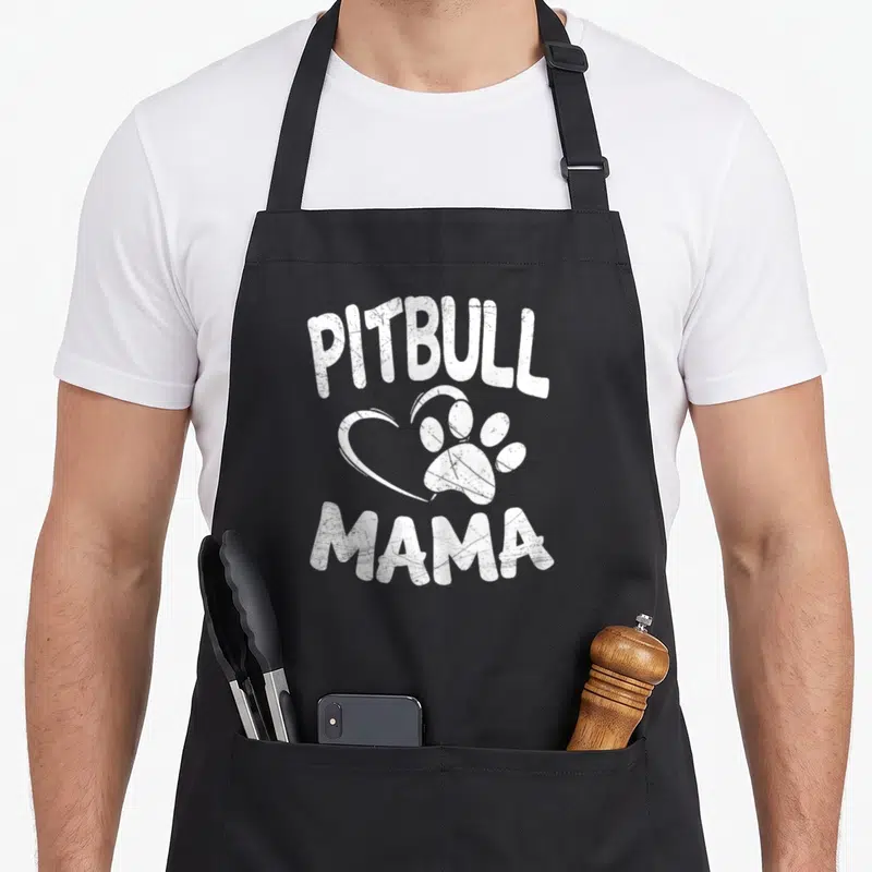 Mama pit dog apron - White distressed PITBULL MAMA text with heart and paw print graphic — shown on a black cotton canvas apron against a white background