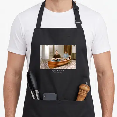 Canoe friends apron - Two men in wooden boat photo with F·R·I·E·N·D·S logo text — shown on a black cotton canvas apron against a white background
