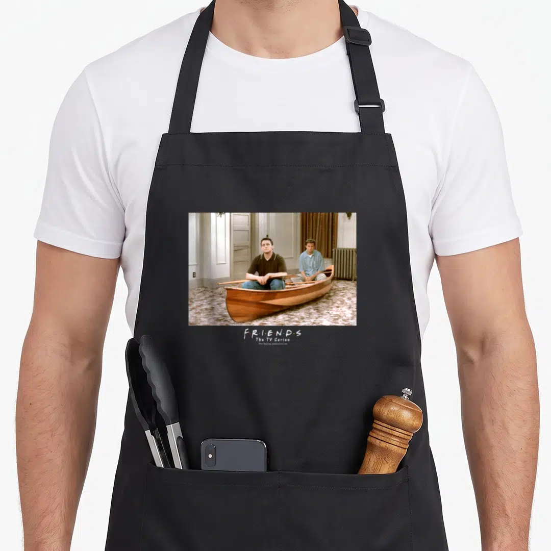 Canoe friends apron - Two men in wooden boat photo with F·R·I·E·N·D·S logo text — shown on a black cotton canvas apron against a white background