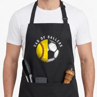 Softball father son apron - Arched Dad of Ballers text over split yellow softball and white soccer ball graphic — shown on a black cotton canvas apron against a white background