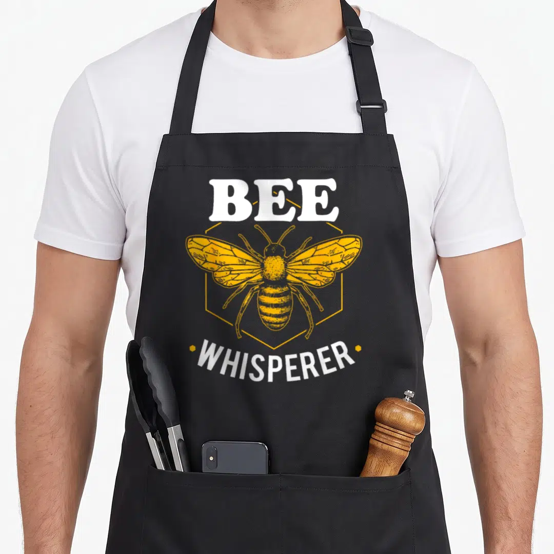 Whisperer bee apron - Yellow bee in hexagon with BEE WHISPERER text in white — shown on a black cotton canvas apron against a white background