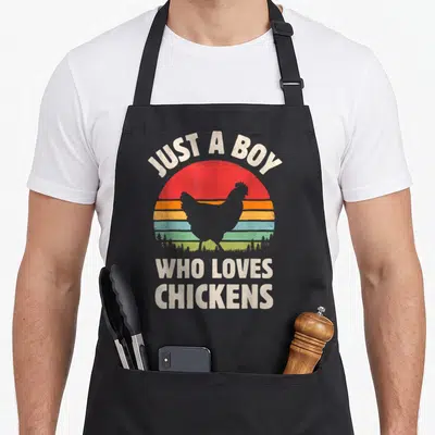 Sunset farmers apron - Retro striped sun with chicken silhouette and text JUST A BOY WHO LOVES CHICKENS above and below — shown on a black cotton canvas apron against a white background