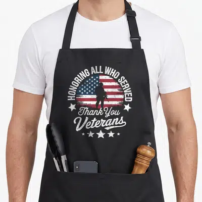 Honoring veterans day apron - Distressed soldier silhouette inside a circular flag with arching HONORING ALL WHO SERVED — shown on a black cotton canvas apron against a white background