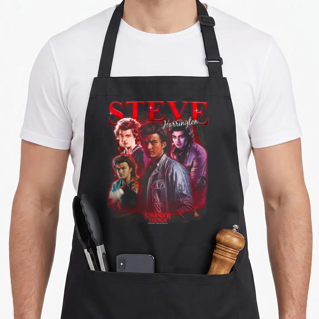 Steve novelty apron - Four portraits of Steve Harrington with red STEVE text and Stranger Things logo — shown on a black cotton canvas apron against a white background
