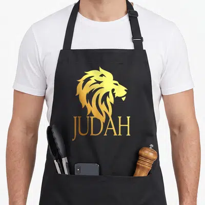 Tribe lions apron - Gold stylized lion head profile above JUDAH text in matching gold font — shown on a black cotton canvas apron against a white background